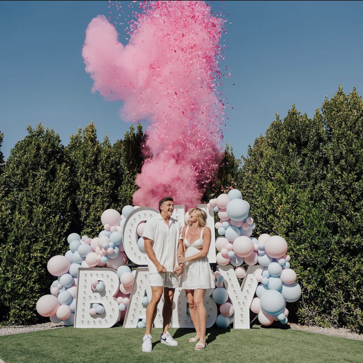 Couple celebrating a gender reveal with pink confetti, pastel balloons and OH BABY marquee letters