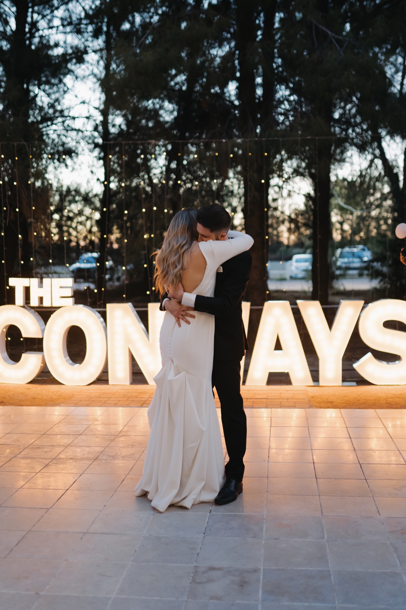 Newlyweds embracing in front of glowing THE CONWAYS marquee letters